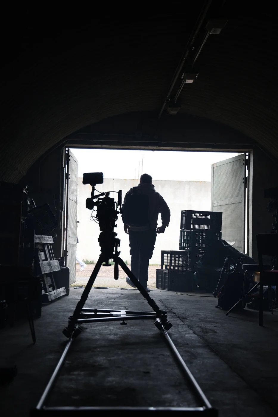A camera on a dolly track inside a dark curved bunker, pointed towards the open doors and daylight beyond